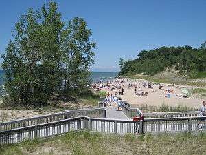 Photograph showing a sandy beach with sunbathers and Lake Ontario in the distance.