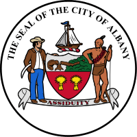 A black circle with white fill is shown with the coat of arms at center. Above the coat of arms, following an arced path, are the letters "The Seal of the City of Albany"
