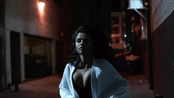 Selena Gomez running in a street at night dressed in an ivory sweater.