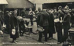 Rescue workers and police standing at the pithead. Some of the men are tending a coffin