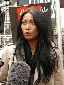A black-haired woman with a grey coat getting interviewed