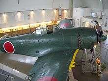Color photo of a dark green single engined monoplane aircraft inside a room