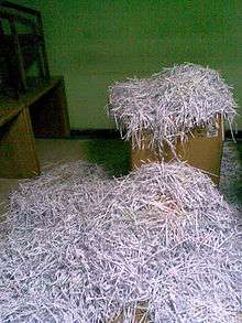 Cardboard box overflowing with shredded paper, with more shredded paper on floor