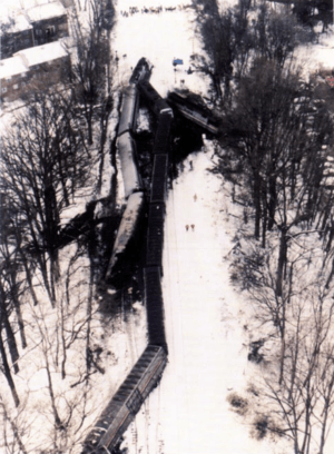 Snow-covered railway line lined by trees. Two wrecked trains.
