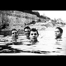 A black-and-white photograph of Slint standing in tall water with only part of their faces visible
