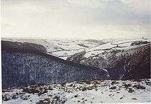 A thin covering of white snow with rocks poking through it, covering sloping hillsides.