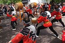 Performers from the group Soh Daiko perform outdoors on various drums in front of an audience.