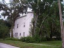 a two story square building partially obscured by oak trees