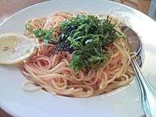 A white bowl of spaghetti in red sauce, ganished with minced nori and julienned shiso leaves
