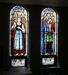 Two stained-glass windows: left, a barefoot woman in an apron; right, a bearded man in armor with a sword and shield