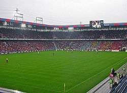 A football match taking place at a sold-out stadium. The sky is cloudy and gray.