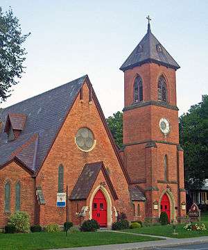 A brick church with steep slate roof, red doors and a tower