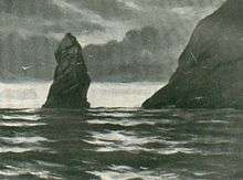 A huge fang-like sea stack jutting from the sea.