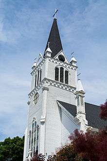 A white church steeple, with a black pointed roof.