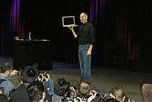 Man in black shirt and jeans holding tablet computer on stage