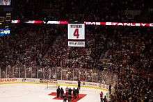 A large white banner with the number 4 is suspended in air above an ice hockey rink, as the crowd cheers.