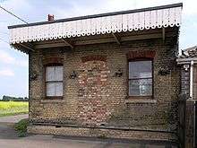 small disused railway station looking from the other side of the track two windows bricked-up doorway roof bordered by white painted edges