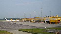 A mostly yellow airport terminal seen from the apron; furthest away there are two jet planes parked