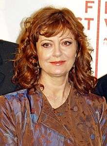 Upper torso of a red-haired female with a dark green shirt underneath a brown and blue jacket.