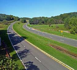 A divided highway with gentle curved roadways receding into a countryside of rolling hills
