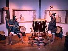 A display at the Osaka Human Rights Museum depicting two workers, wielding large mallets, in the process of applying appropriate tension to a taiko.