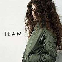 Lorde looking down with her face partially obscured by long curly dark hair, wearing a khaki-coloured bomber jacket and the text "TEAM"