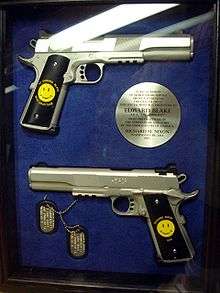 A case with two handguns, both with a stamped Smiley Face - one of the guns has "To Edward Blake, With Gratitude" around the Smiley, while the other has "Richard Nixon - 1976" -, dogtags, and a circular plaque, written by Richard Nixon, stating they are a gift to the Comedian in recognition for his services.