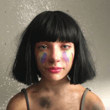 The artwork portrays the head and shoulders of a teenage girl wearing a black bobbed wig, with rainbow colours on her cheeks