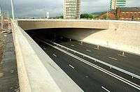 Empty motorway underpass with three lanes either side of the central barrier.