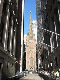 Ground-level view of a large, brown church with Gothic architecture and a tall, tapering spire that is only partially visible in the image