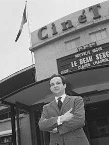 Black-and-white photo of man in a suit outside a movie theater with his arms folded