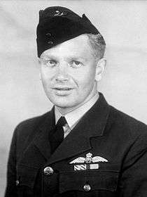 Formal head-and-shoulders portrait of man in dark military uniform with pilot's wings on breast pocket, wearing a forage cap