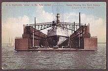 picture of a large battleship from rear inside a giant floating box-like structure in a harbor