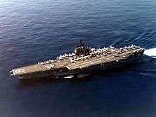 Large aircraft carrier with numerous aircraft on its flight deck.