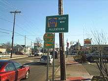 A road approaching a signalized intersection in a commercial area. A green sign on the right side of the road reads County Route 539 north left arrow Allentown with a shield pointing left to the Garden State Parkway below it