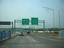 A multilane divided highway coming off a bridge with a parallel freeway. A set of two green signs is over the road, with the one on the left reading south U.S. Route 9 Route 35 Sayreville 1/4 mile and the one on the right reading Garden State Parkway south South Amboy Business center right lane 1/4 mile