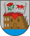 A coat of arms depicting an open book with a red rose on one page and a red bull on the other all hovering over a red heart with a building in the background