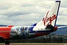 View of aircraft aft fuselage showing advertisements against a red background. The tail contains the underlined word "Virgin".
