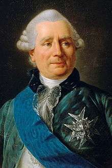 Middle-aged, white-haired man wearing a blue velvet jacket, white shirt, and a chivalric order pinned to his jacket