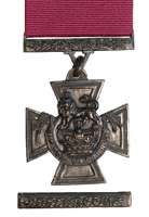 A bronze cross pattée bearing the crown of Saint Edward surmounted by a crowned lion with the inscription FOR VALOUR. A crimson ribbon is attached