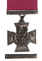 A bronze cross pattée bearing the crown of Saint Edward surmounted by a lion with the inscription FOR VALOUR. A crimson ribbon is attached