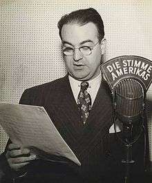 black and white photograph of a male wearing glasses and standing next to a microphone
