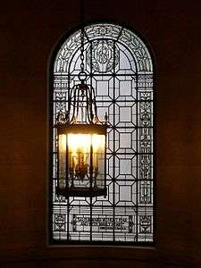 A round-arched window with a complicated iron and glass decoration. A lantern-like light fixture hangs in front. At the bottom of the window is written "Go forward without fear and with manly heart", a quotation attributed to Abraham Lincoln. The words "AD 1919" are also visible in the top of the glass in stylized script.