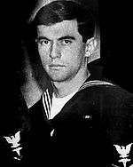 A picture of a man in a United States Navy uniform while looking at the camera with a stern face.