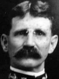 Black-and-white frontal headshot of man with small glasses and a neatly trimmed mustache. The edge of a Navy uniform is around his neck.