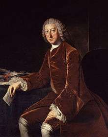 An oil painting of William Pitt the Elder wearing a red velvet suit and powdered wig, seated at a desk and holding a letter.