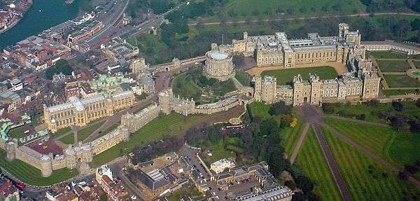 An aerial photograph of a Windsor Castle, with three walled areas clearly visible, stretching left to right. Straight roads stretch away in the bottom right of the photograph, and a built-up urban area can be seen outside the castle on the left.