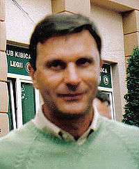 An out-of-focus portrait shot of a dark-haired man in a lime-green v-neck sweater.