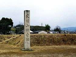 Modern stele with Japanese characters next to a raised platform.