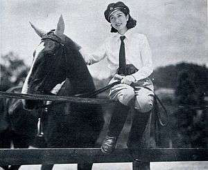 Yukiko sits on a fence with one arm around a horse
